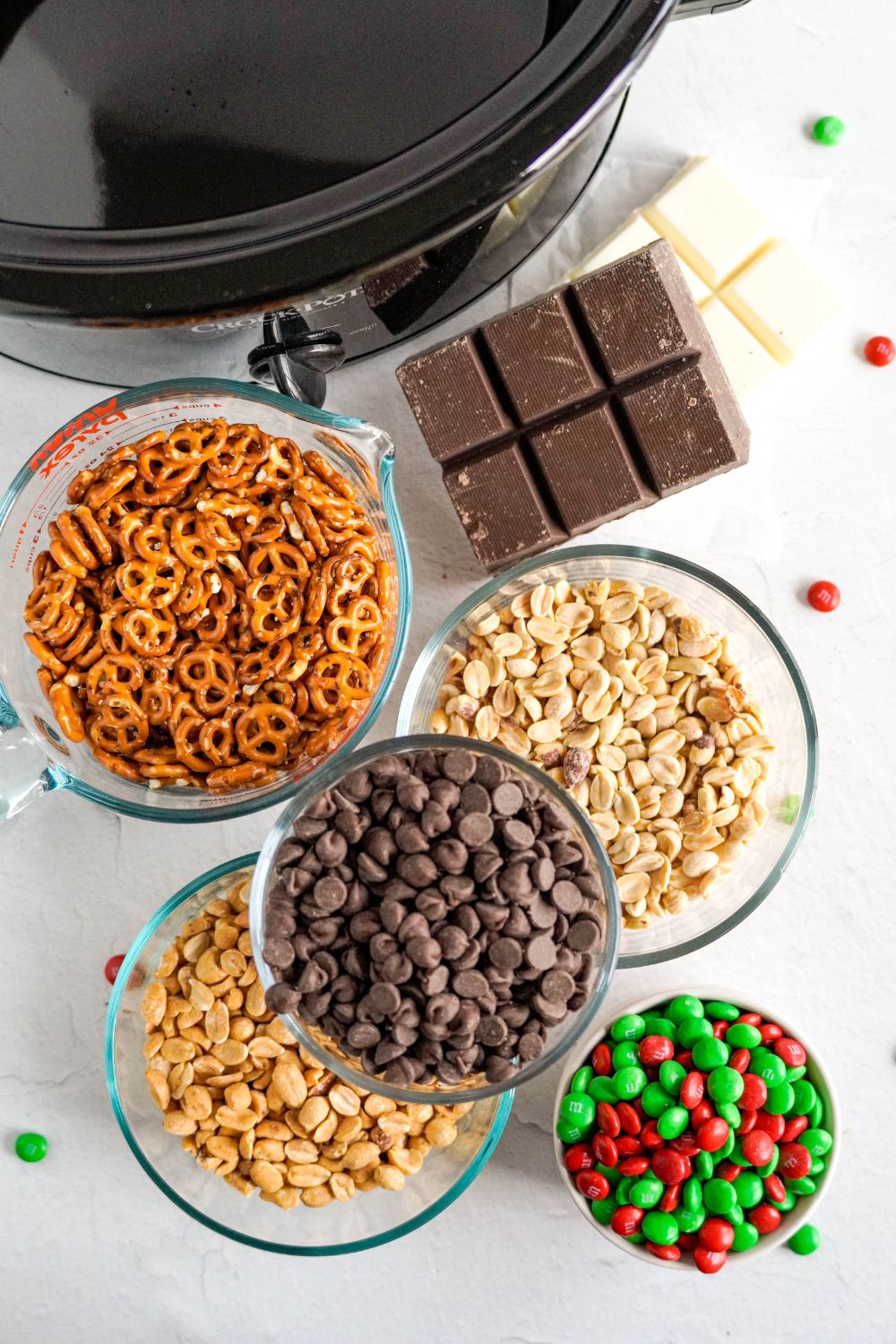 crockpot with bowls of all the ingredients to make Crockpot Chocolate Pretzel Christmas Candy