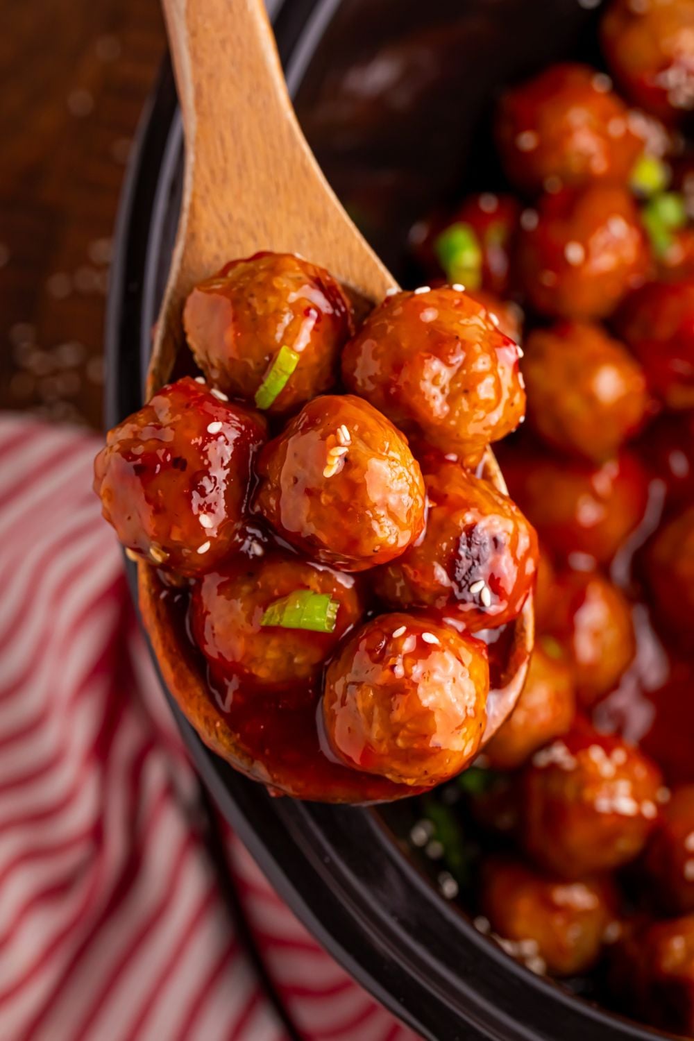 wooden spoon full of crockpot meatballs above the crockpot with a red striped towel beside it