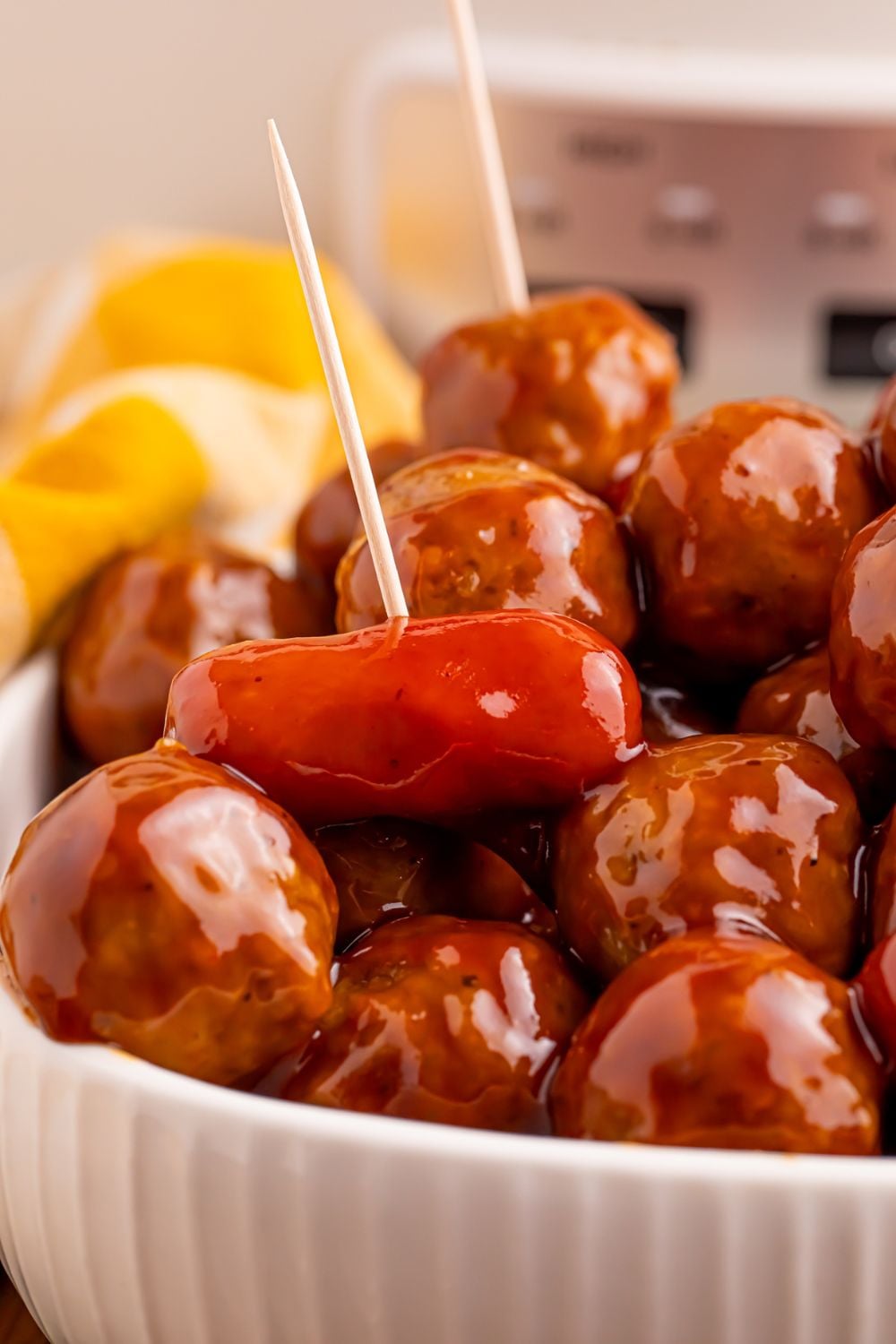 Crockpot Teriyaki BBQ Cocktail Meatballs & Lil Smokies mixture in a white bowl on table with a yellow towel behind it on the table 