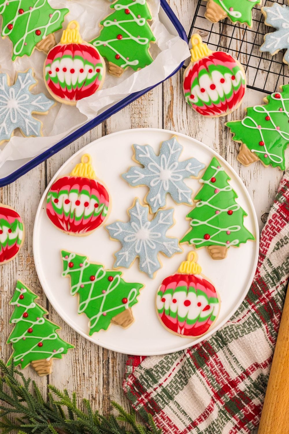 a white plate with a mix of Decorated Sugar Cookies for Christmas on it, and then a tray with more cookies next to it on the table