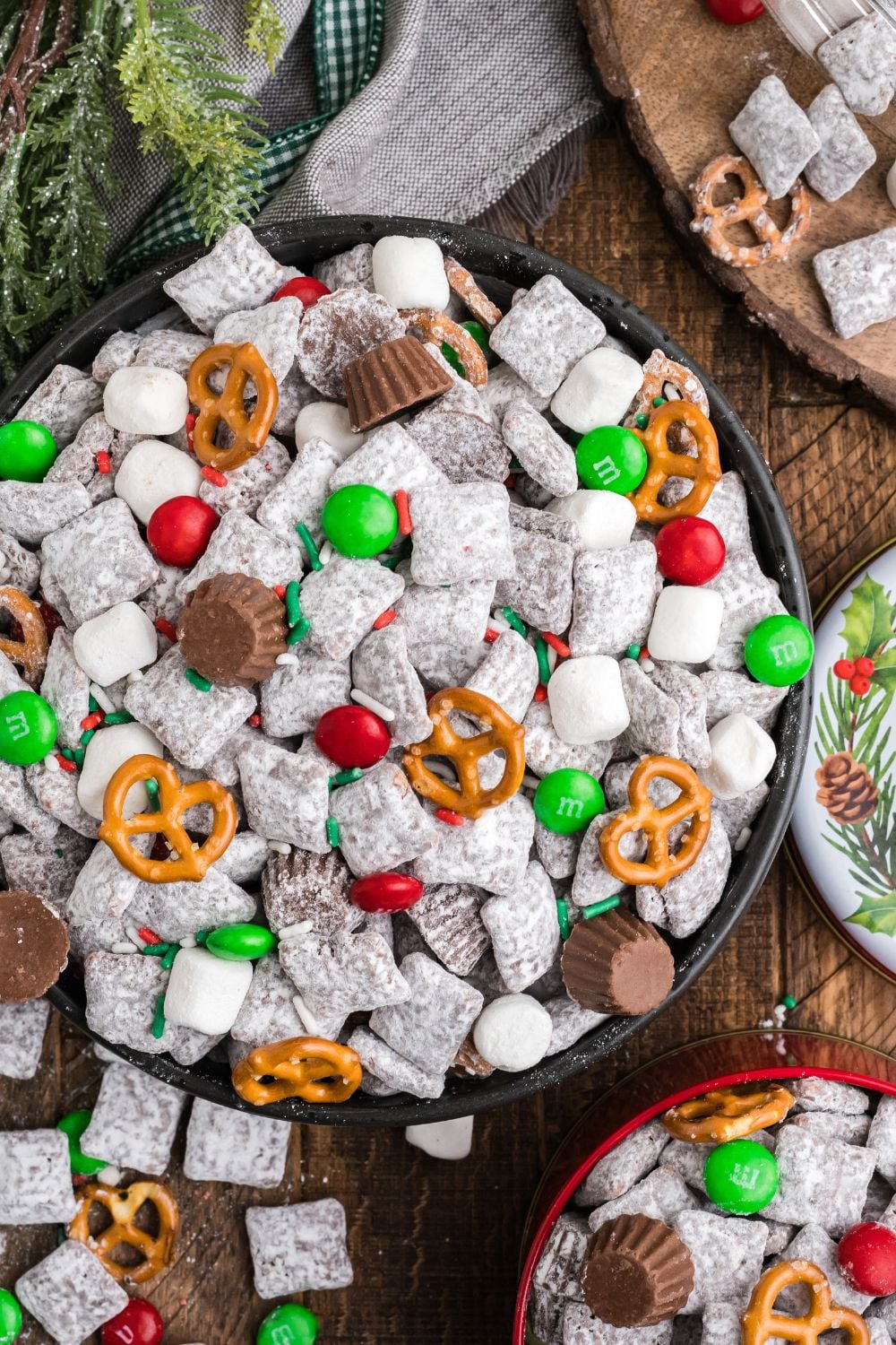 Christmas Chex Mix in a large bowl on table overflowing on wooden table with smaller bowls around table with more