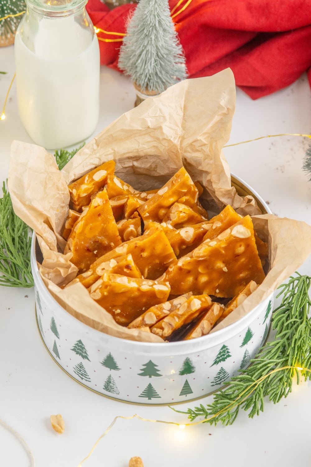 tin full of peanut brittle with a red towel behind it