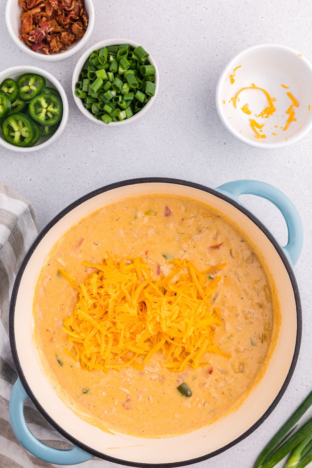 shredded cheese poured over the top of the jalapeño popper crack chicken soup in a pot on a table