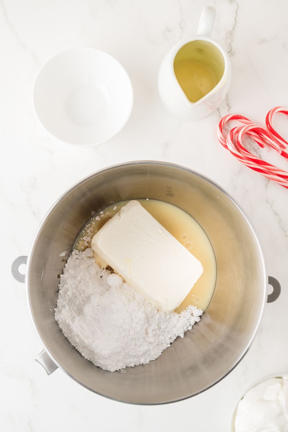 cream cheese, powdered sugar and more in a metal container on table with candy canes and more around 