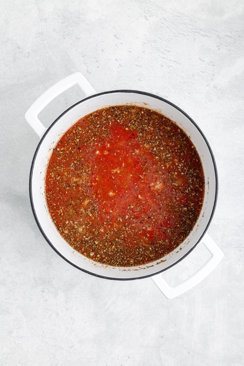 tomato mixture and spices in a white pot on table for making Sausage Tortellini Soup