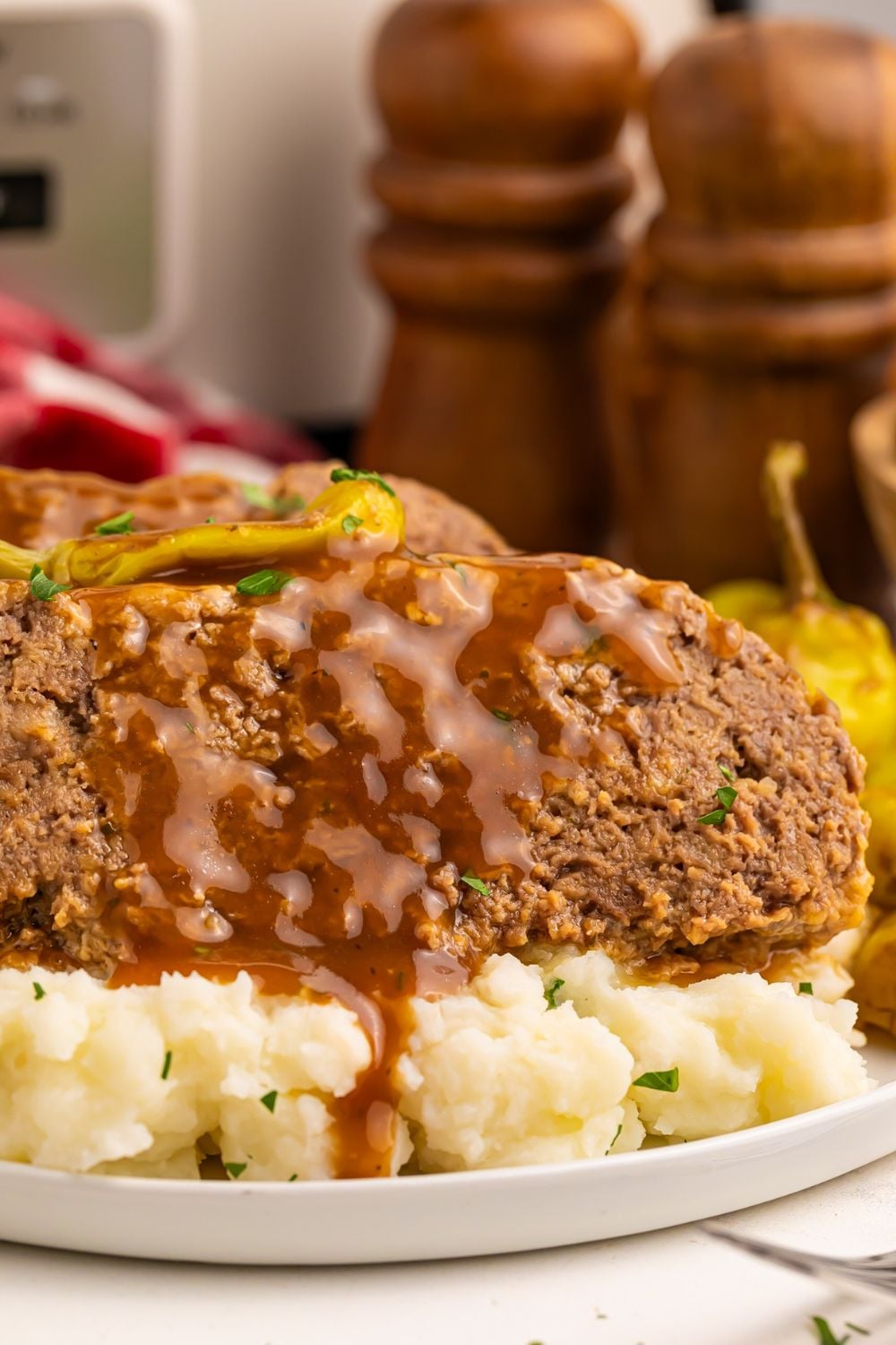 mashed potatoes on a plate with slices of meatloaf on top with gravy drizzling down the meatloaf