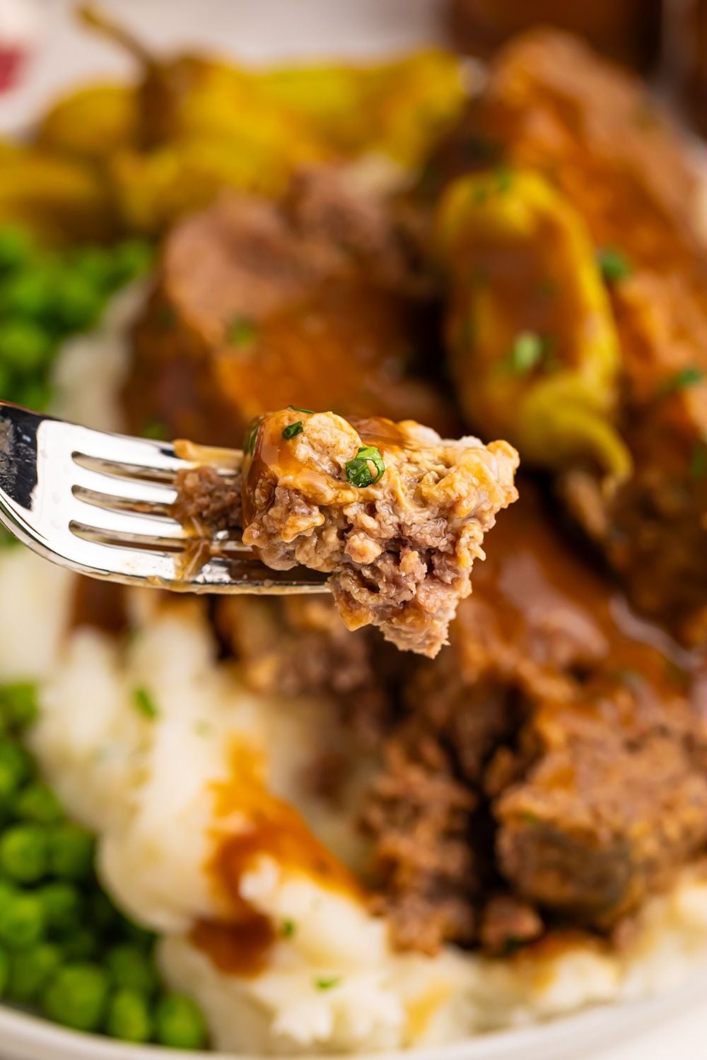 a plate full of Crockpot Mississippi Meatloaf with mashed potatoes and green peas with a fork with a bite of the meatloaf on it