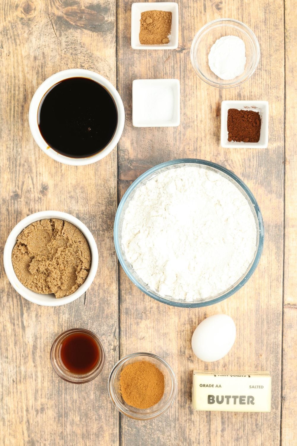 all the ingredients for Christmas gingerbread cookies on a wooden table in single serve bowls 