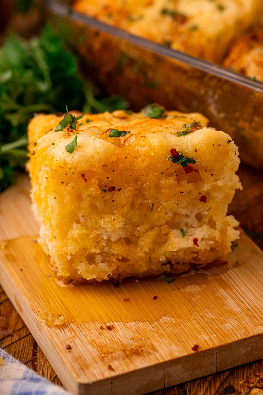 Cowboy Butter Swim Biscuit on a wooden cutting board with butter poured all over the top and the glass pan with the rest of the biscuits to the side