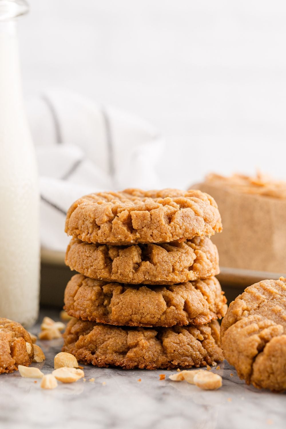 stack of peanut butter cookies with nuts all around it and glass of milk to the side of the cookies