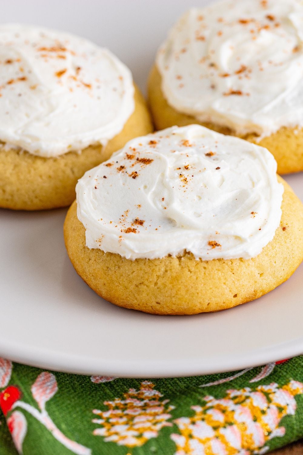 white plate with three Soft Frosted Eggnog Cookies placed on it and a green holiday napkin under the plate
