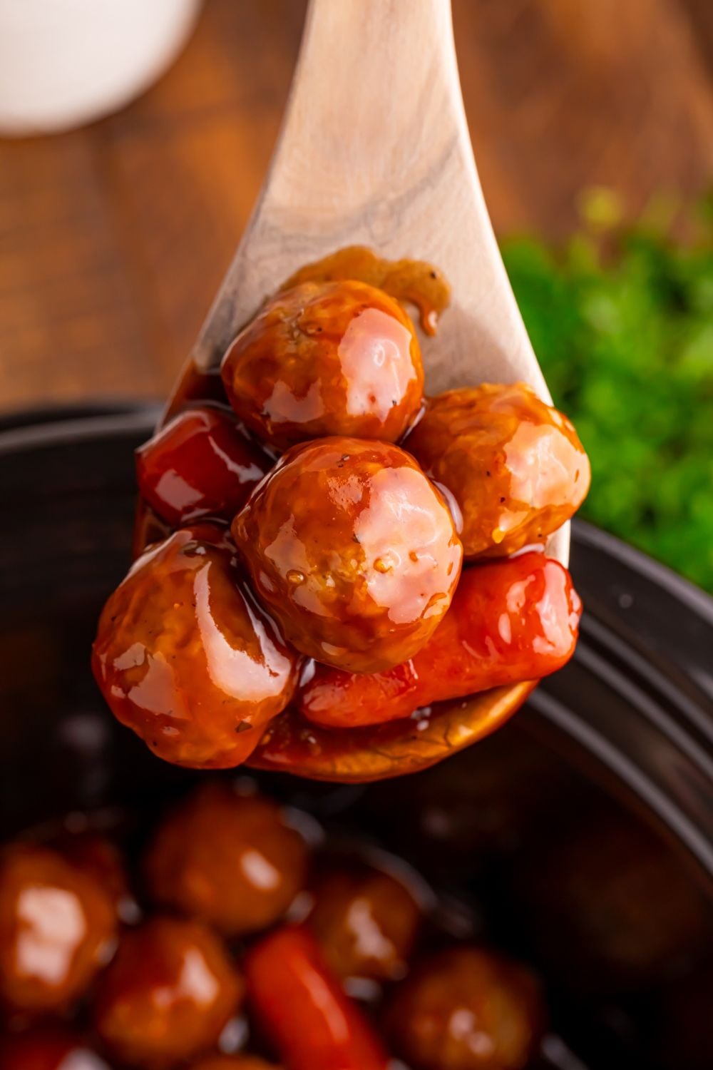 Crockpot Teriyaki BBQ Cocktail Meatballs & Lil Smokies on a wooden spoon with a black Crockpot under it on the table 