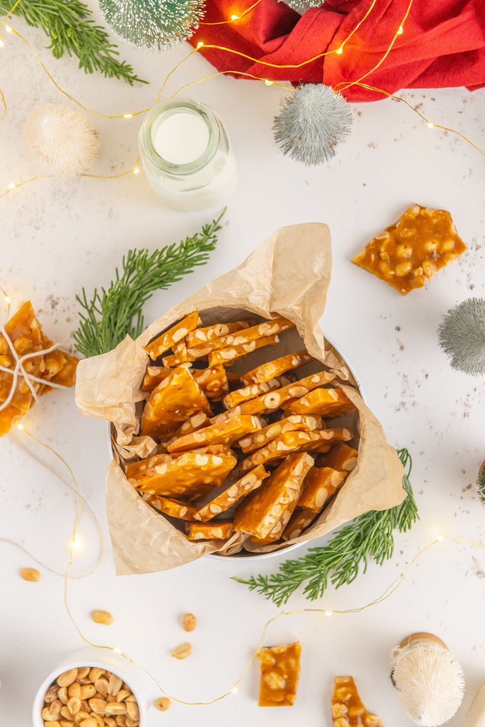 tin on white table with Christmas decor full of Homemade Peanut Brittle