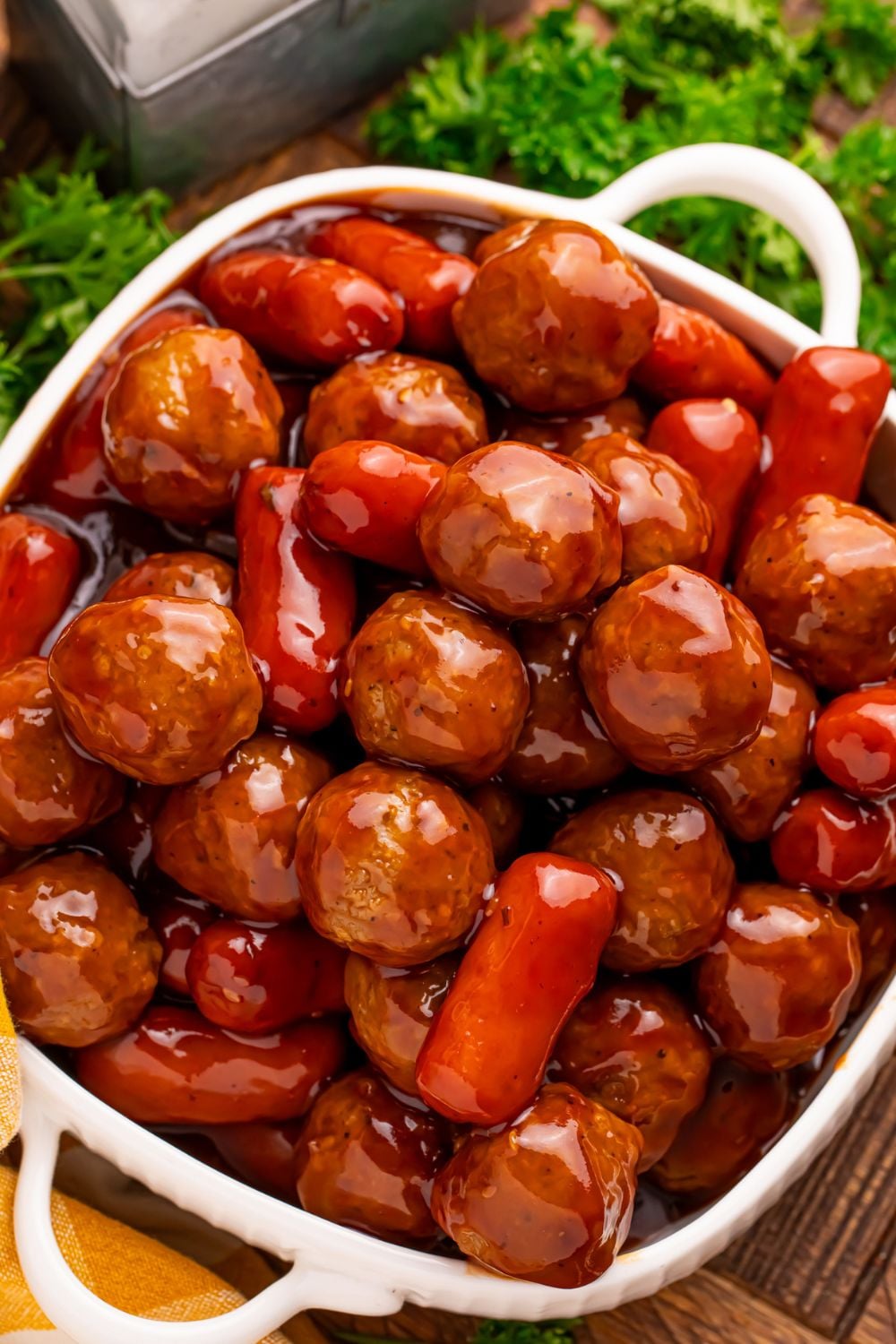 Crockpot Teriyaki BBQ Cocktail Meatballs & Lil Smokies in a white casserole pan on table with fresh parsley around it on the table for garnish 
