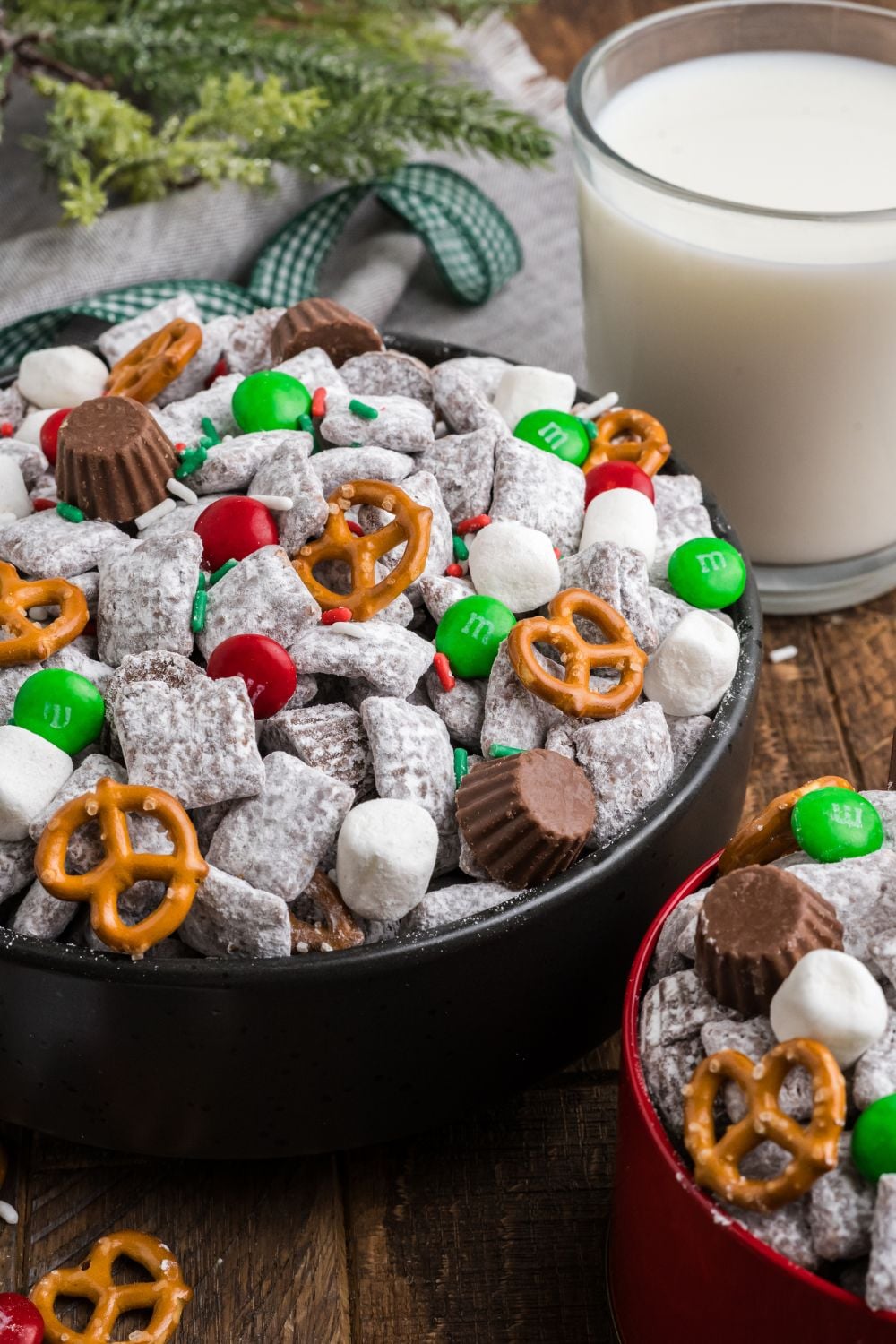 Christmas Chex Mix in a black bowl on table with a glass of milk to side