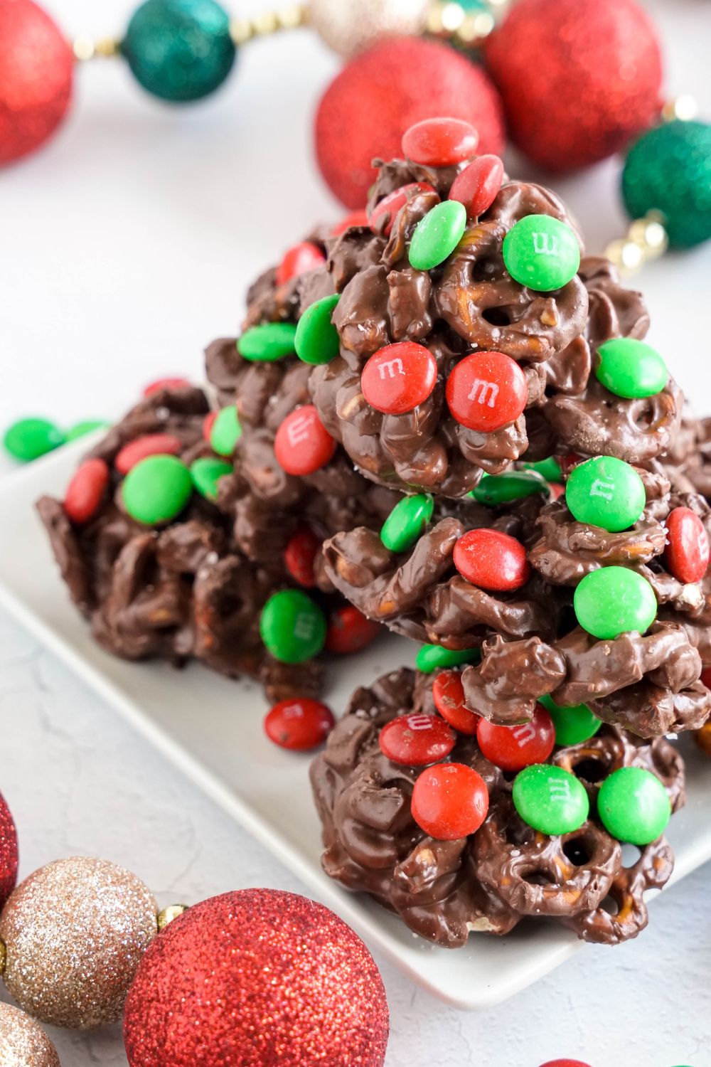 Crockpot Chocolate Pretzel Christmas Candy stacked on a white plate with Christmas ornament around the table