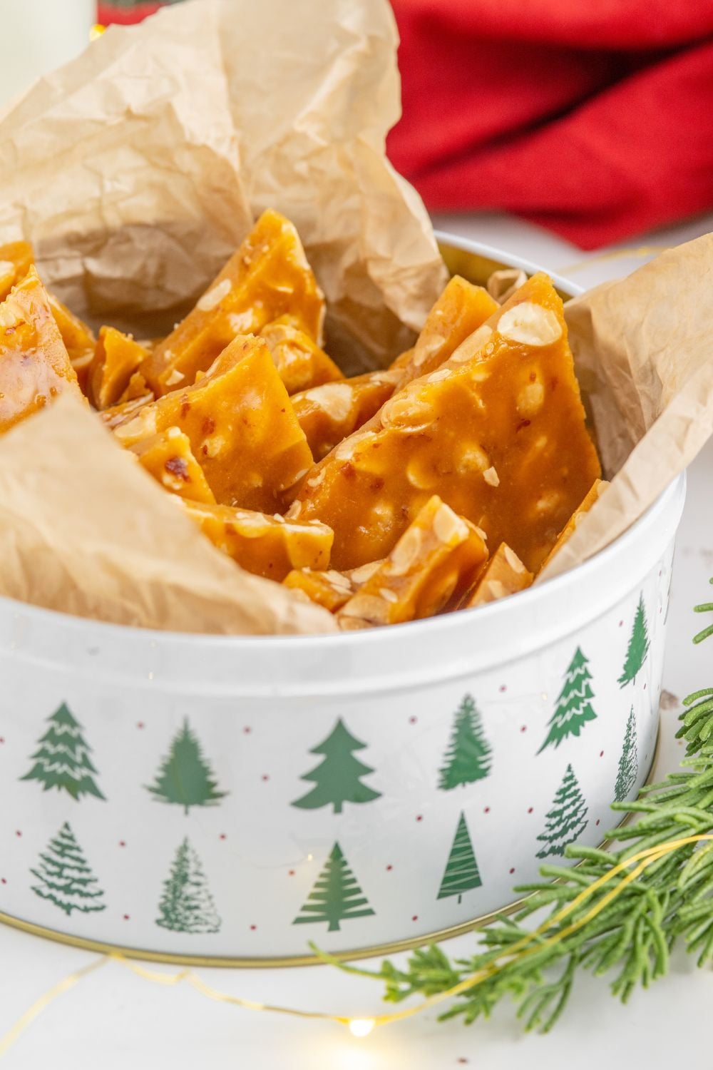 Homemade Peanut Brittle in a Christmas tin on a white counter