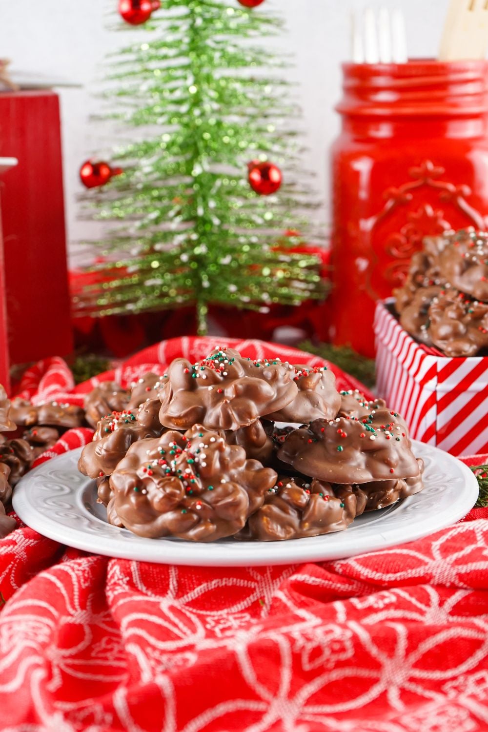 red Christmas themed table with Crockpot Christmas Candy on a white plate and red striped candy tin to side