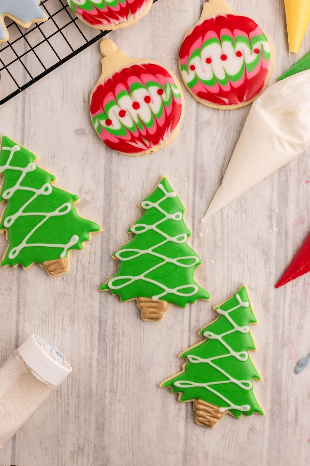 Decorated Sugar Cookies on table that are shaped like Christmas trees piping on a string of lights
