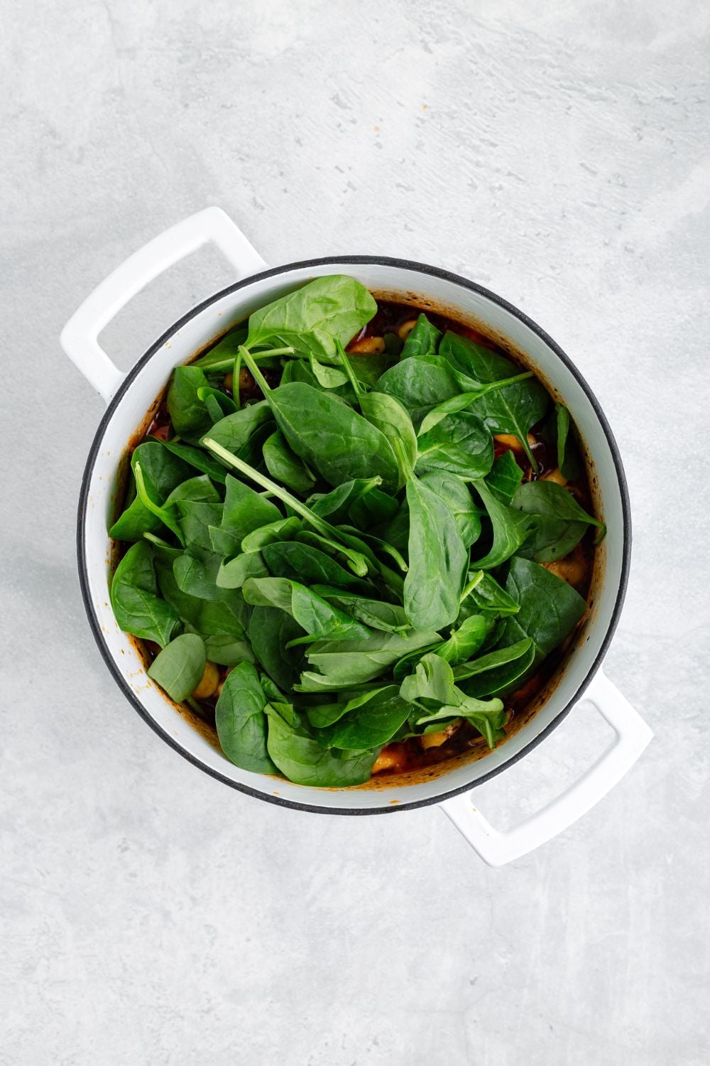 fresh spinach on top of a pot full of Sausage Tortellini Soup