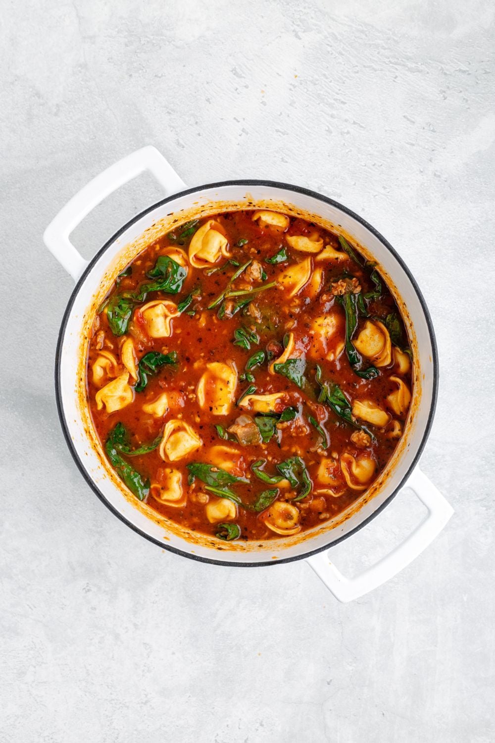 Sausage Tortellini Soup in a white pot sitting on a white counter