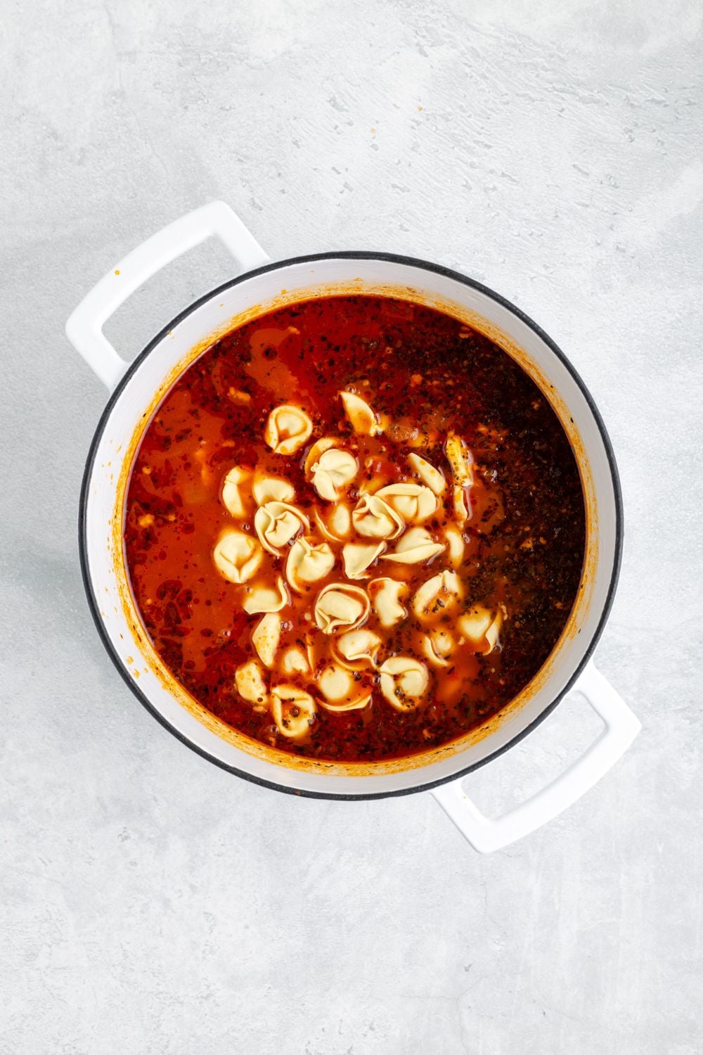 tortellini poured into a white pot on the table for making Sausage Tortellini Soup