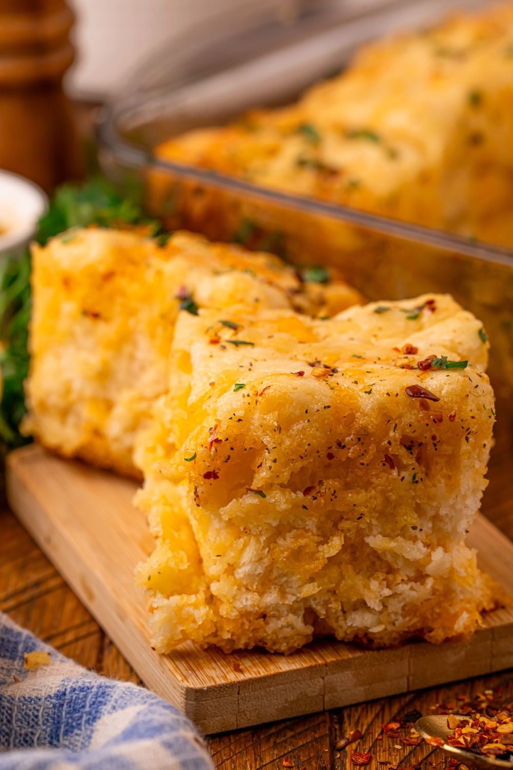 Cowboy Butter Swim Biscuits sliced and placed on a cutting board with the glass pan full of the rest of the biscuits behind the table