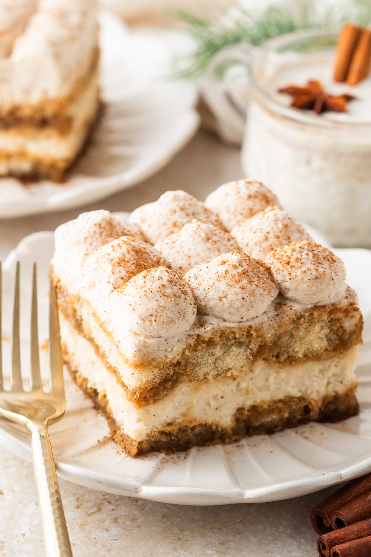 No Bake Eggnog Tiramisu sliced on white serving plates with a glass of eggnog behind the plate 
