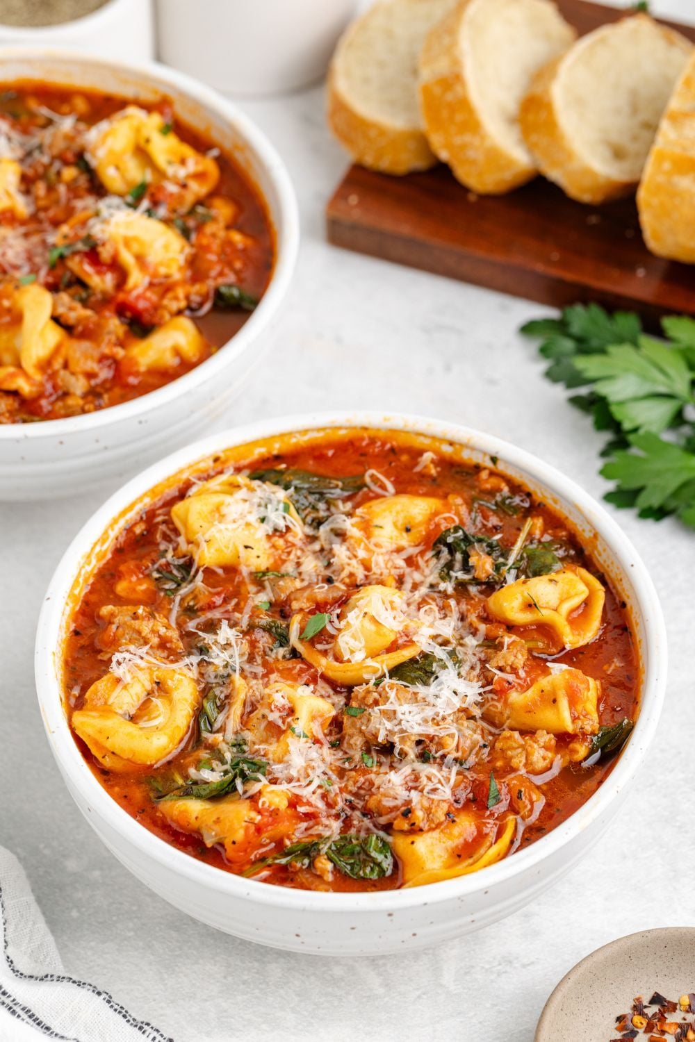white bowls full of Sausage Tortellini Soup on table with a cutting board full of sliced french bread to side