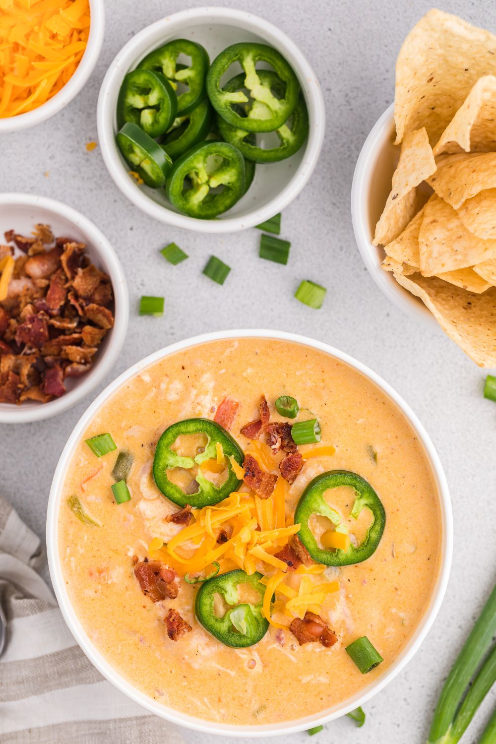 jalapeño popper crack chicken soup in a bowl with small bowls of back, jalapenos, and chips and cheese