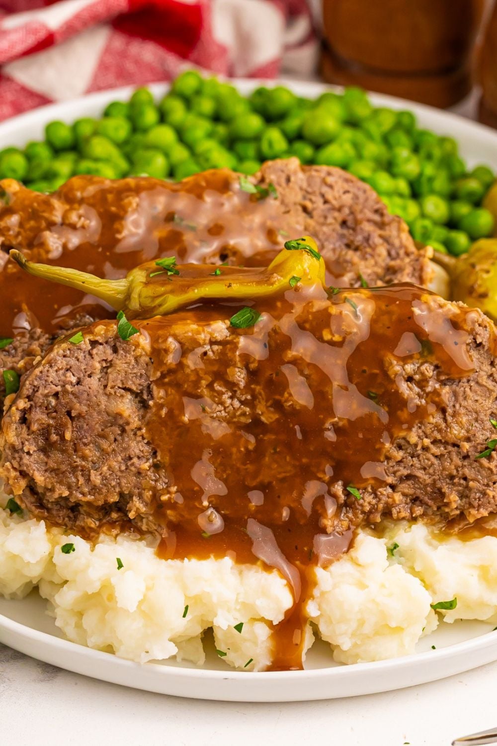 Crockpot Mississippi Meatloaf sliced on top of mashed potatoes and peas on the plate