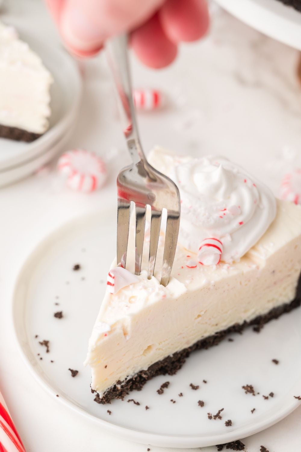 white plate with a slice of No Bake Peppermint Cheesecake on it with a fork poking into the cake 