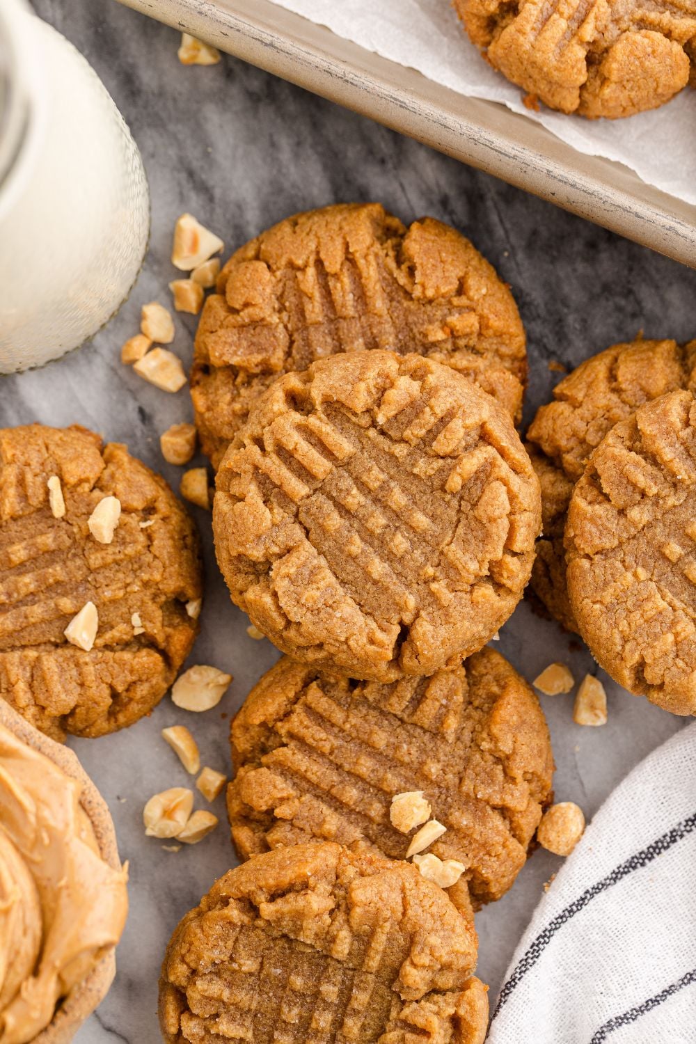 4 Ingredient Peanut Butter Cookies spread around the table with a tall glass of milk in a jar with a try with more cookies to side