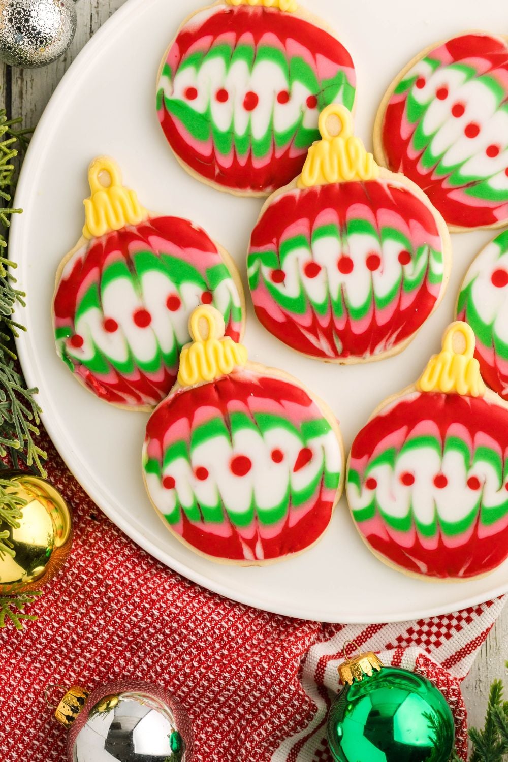Decorated Sugar Cookies on a white plate with Christmas ornaments around the table for a holiday themed look