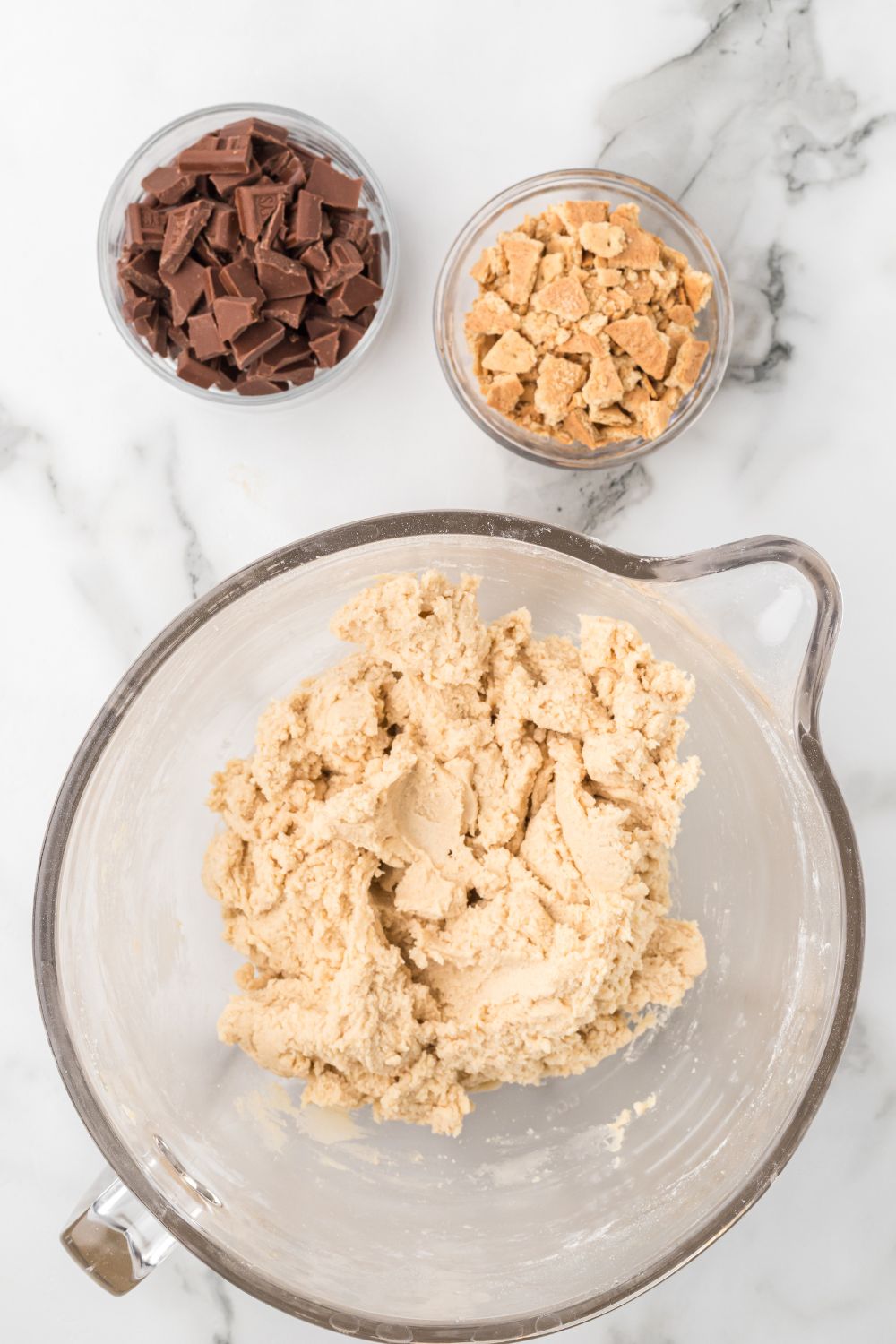 glass bowl for smore cookies on table with a bowl of crushed graham crackers and chocolates to side