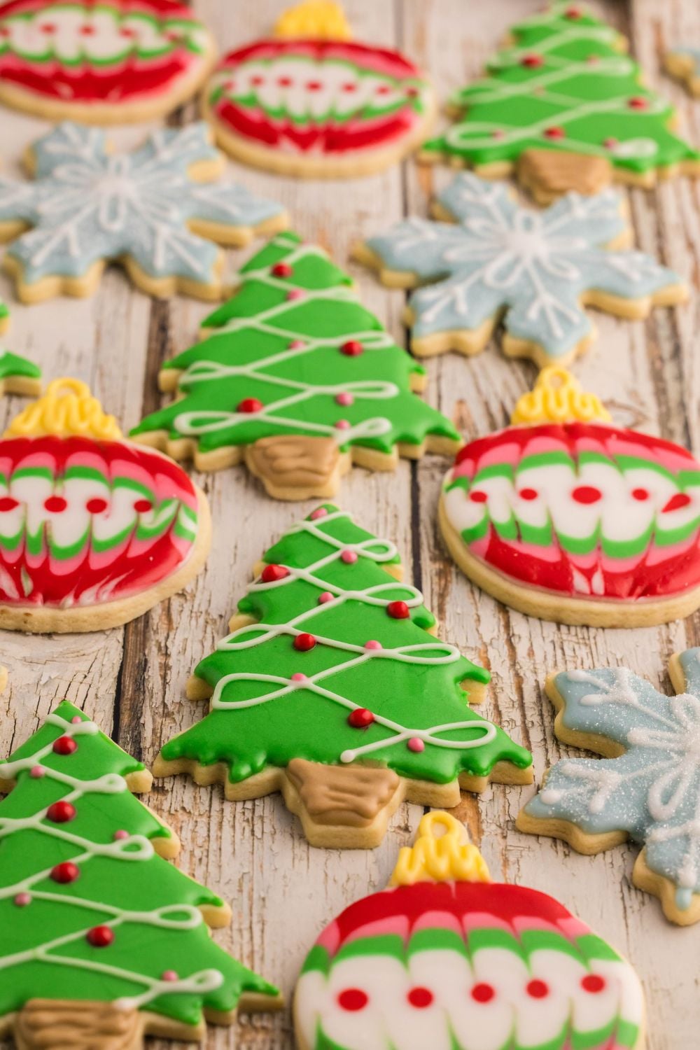 Decorated Sugar Cookies spread out on a table, some look like snowflakes, trees, and ornaments