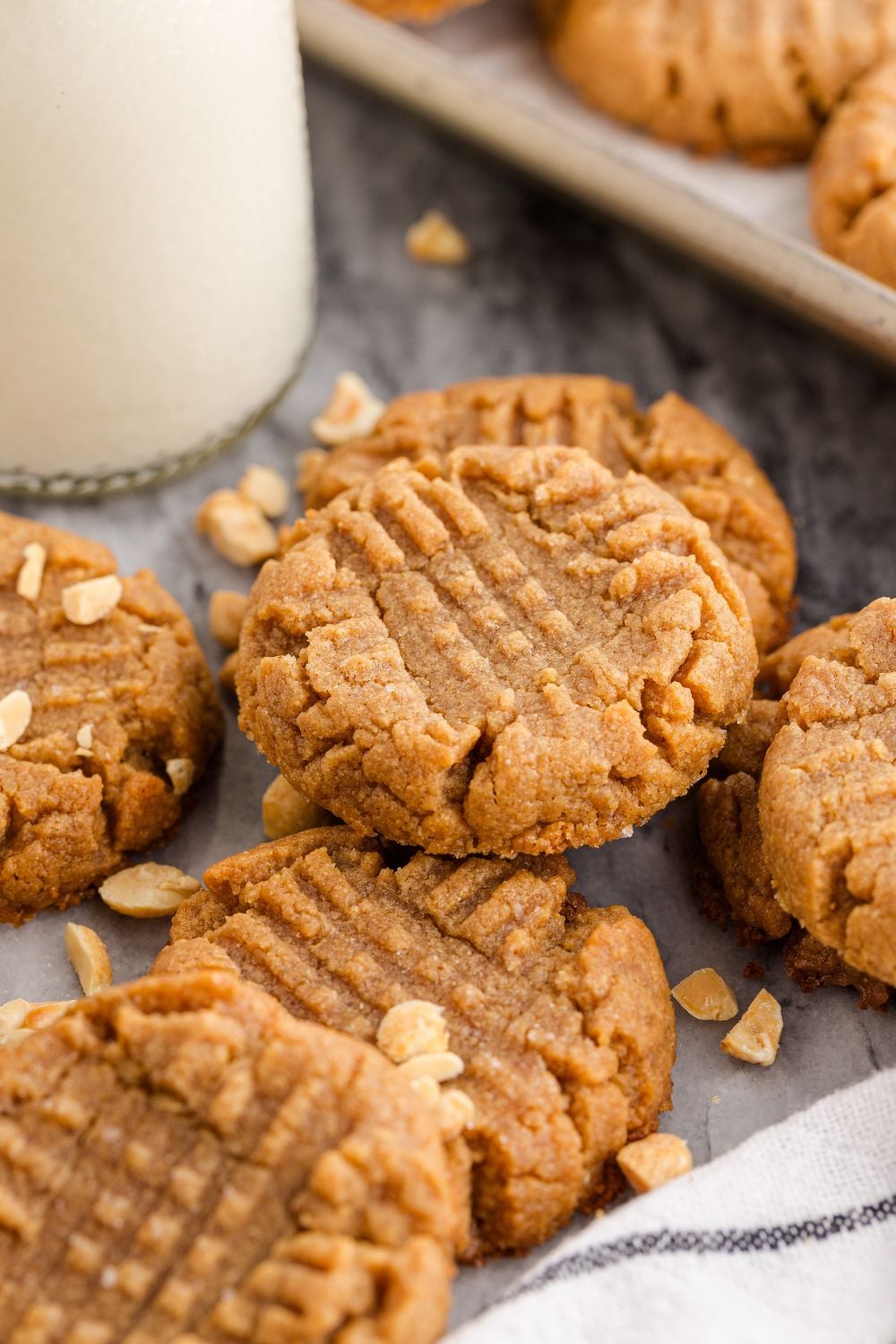 4 Ingredient Peanut Butter Cookies spread around table with a tray full of cookies behind and a tall jar of milk
