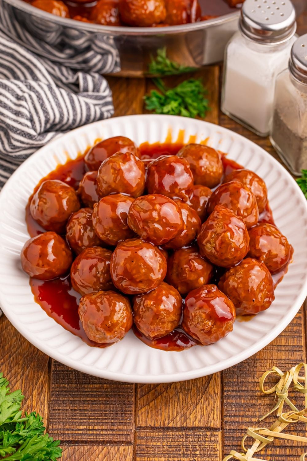 white plate on wooden table full of Peach BBQ Meatballs and toothpicks in front and a skillet with more meatballs behind it on table