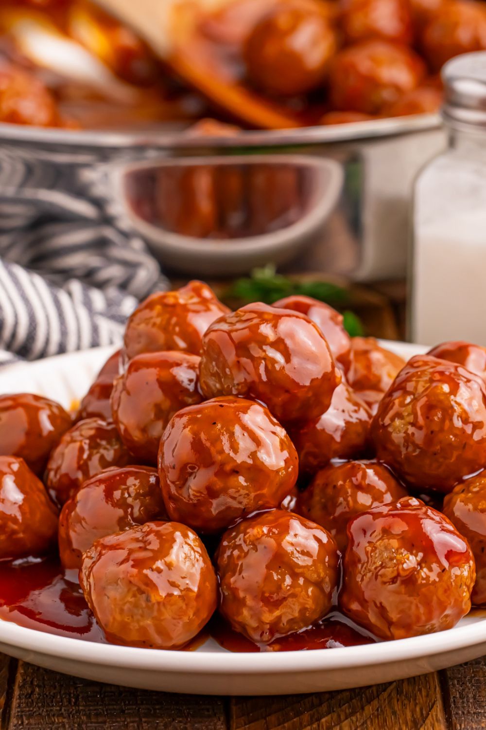 Peach BBQ Meatballs on a white plate on table with a skillet behind it on table with salt shaker to side and a towel