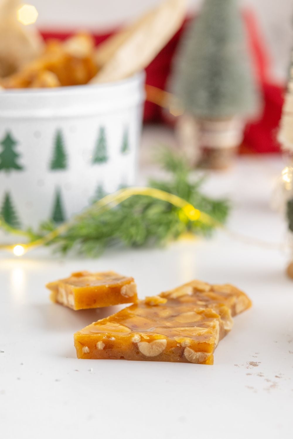 Homemade Peanut Brittle on a white table with Christmas decor behind it on table