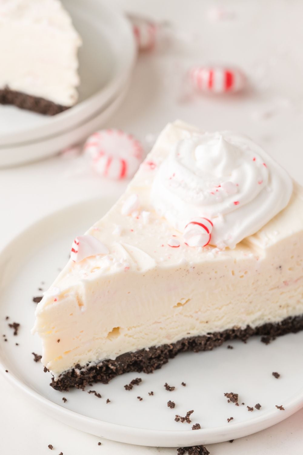 slice of No Bake Peppermint Cheesecake on a white plate with candy around it on table 