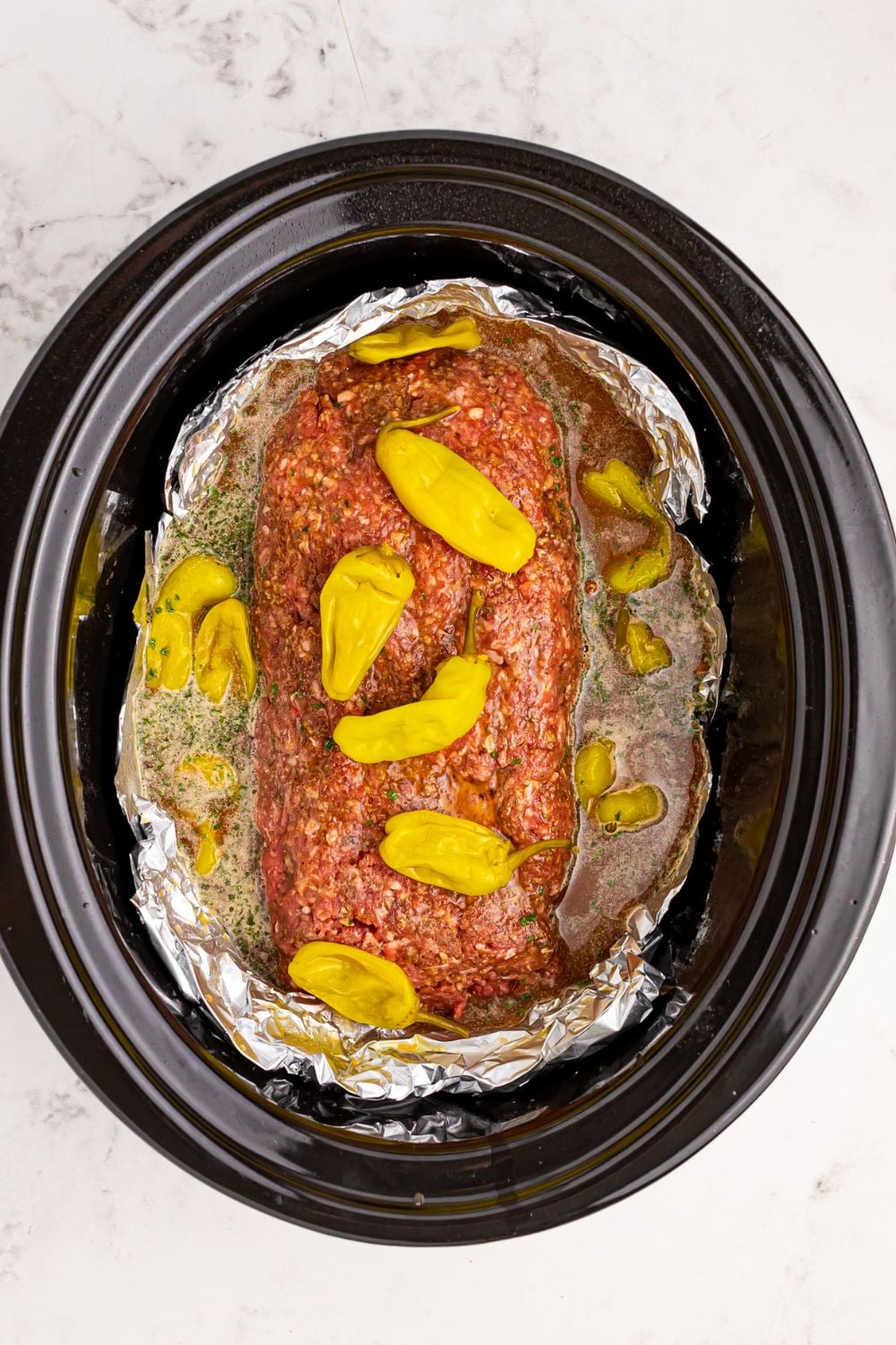peppers on top of meatloaf in a slow cooker with foil