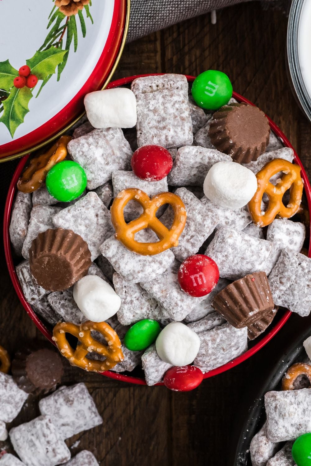 powdered sugar Chex mix in a metal gift tin with lid to side and more of the snack mix placed around the table