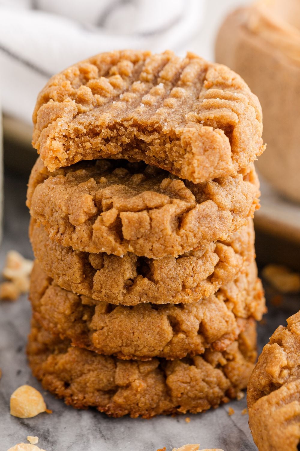stack of peanut butter cookies on table with a bite taken out of the cookie with peanuts scattered around the table