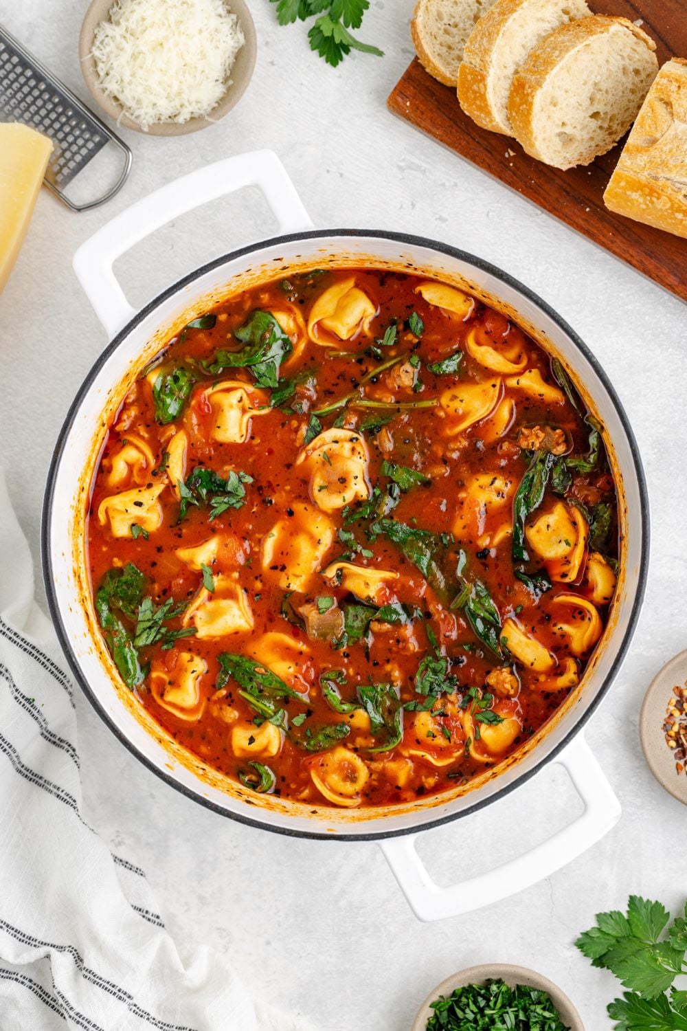 Sausage Tortellini Soup in a stockpot sitting on a marble counter with some bread and grated parmesan to the side