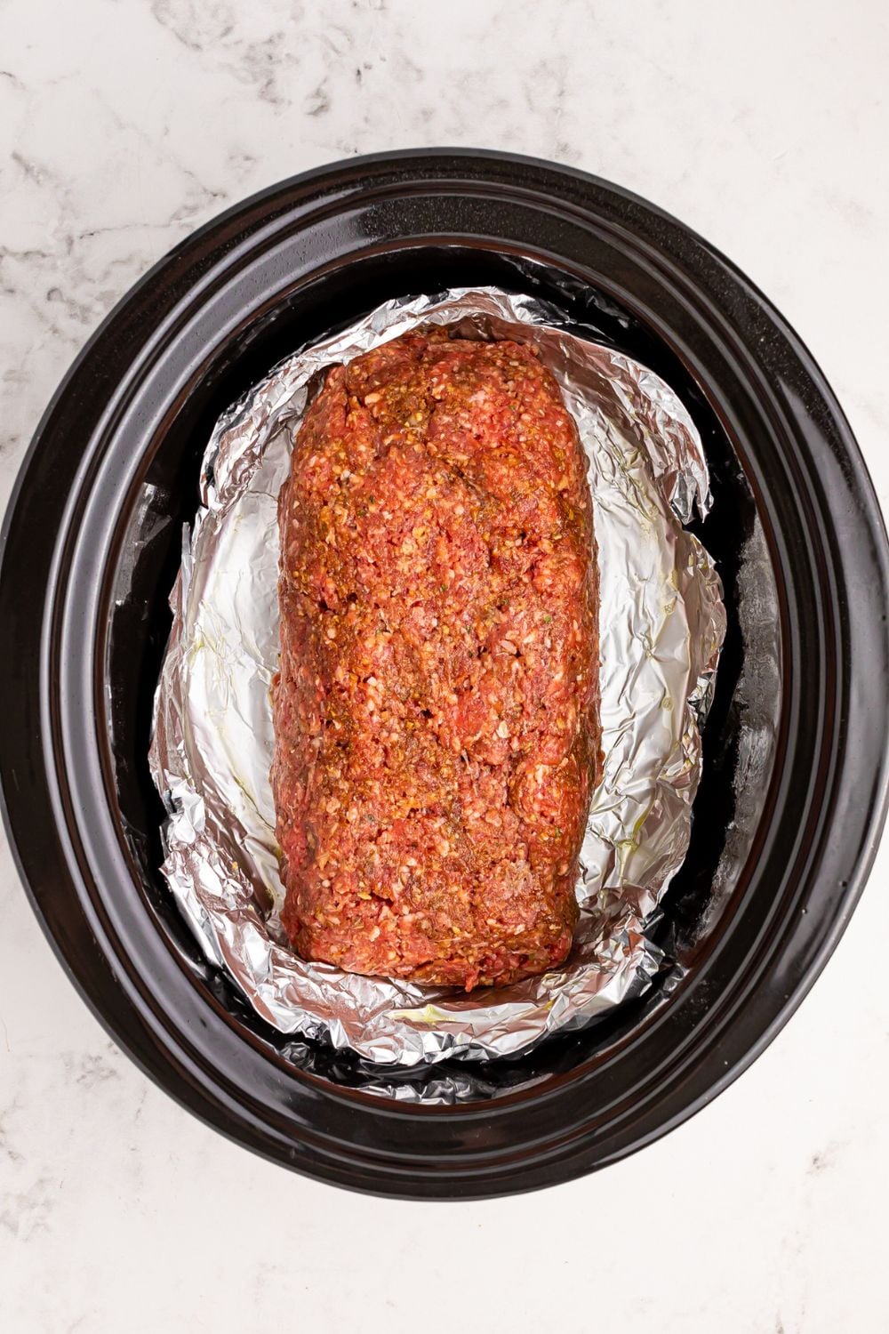 black crockpot on table with foil and a meatloaf log in center of crockpot