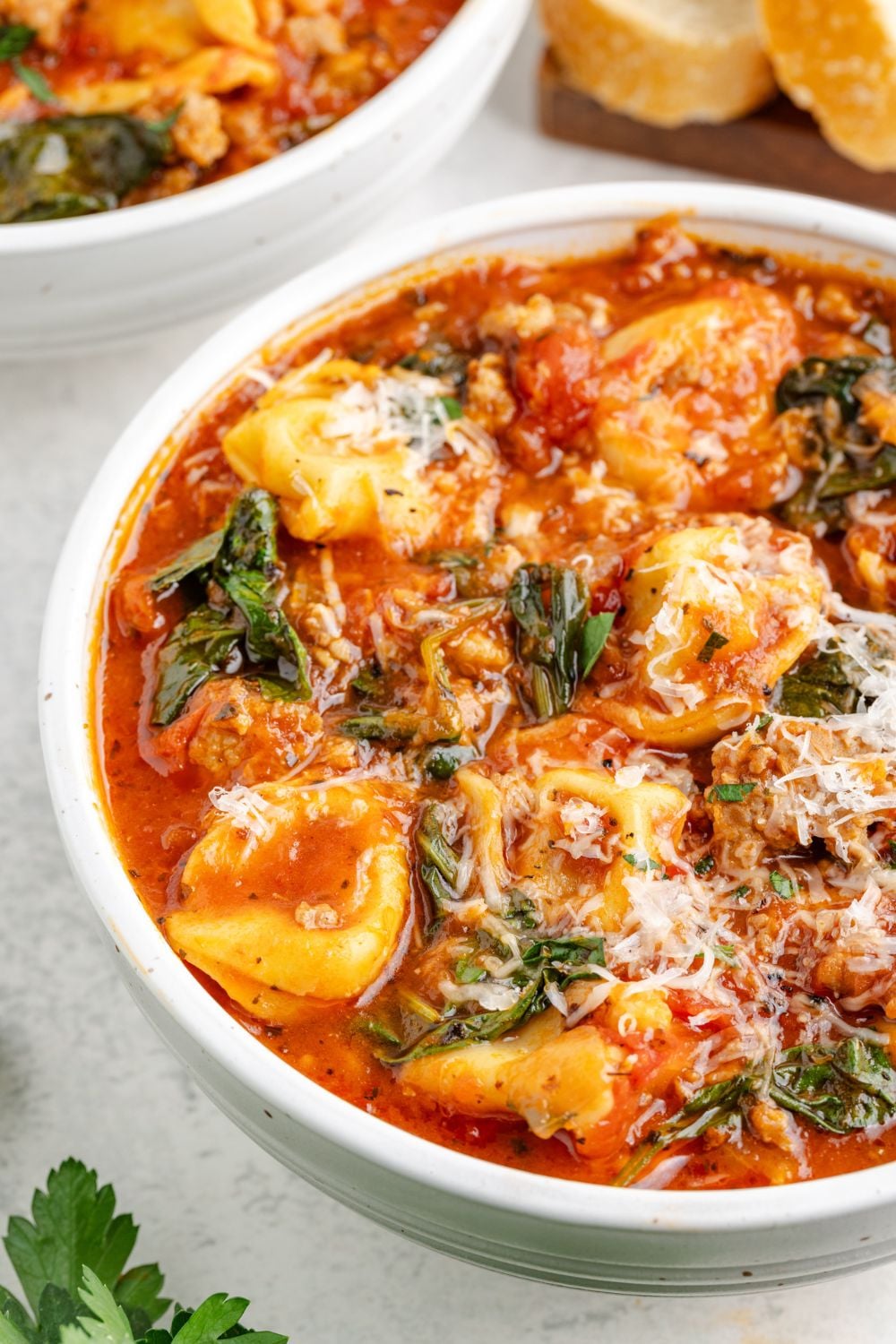 side view of a white bowls on table full of Sausage Tortellini Soup and topped with grated parmesan cheese