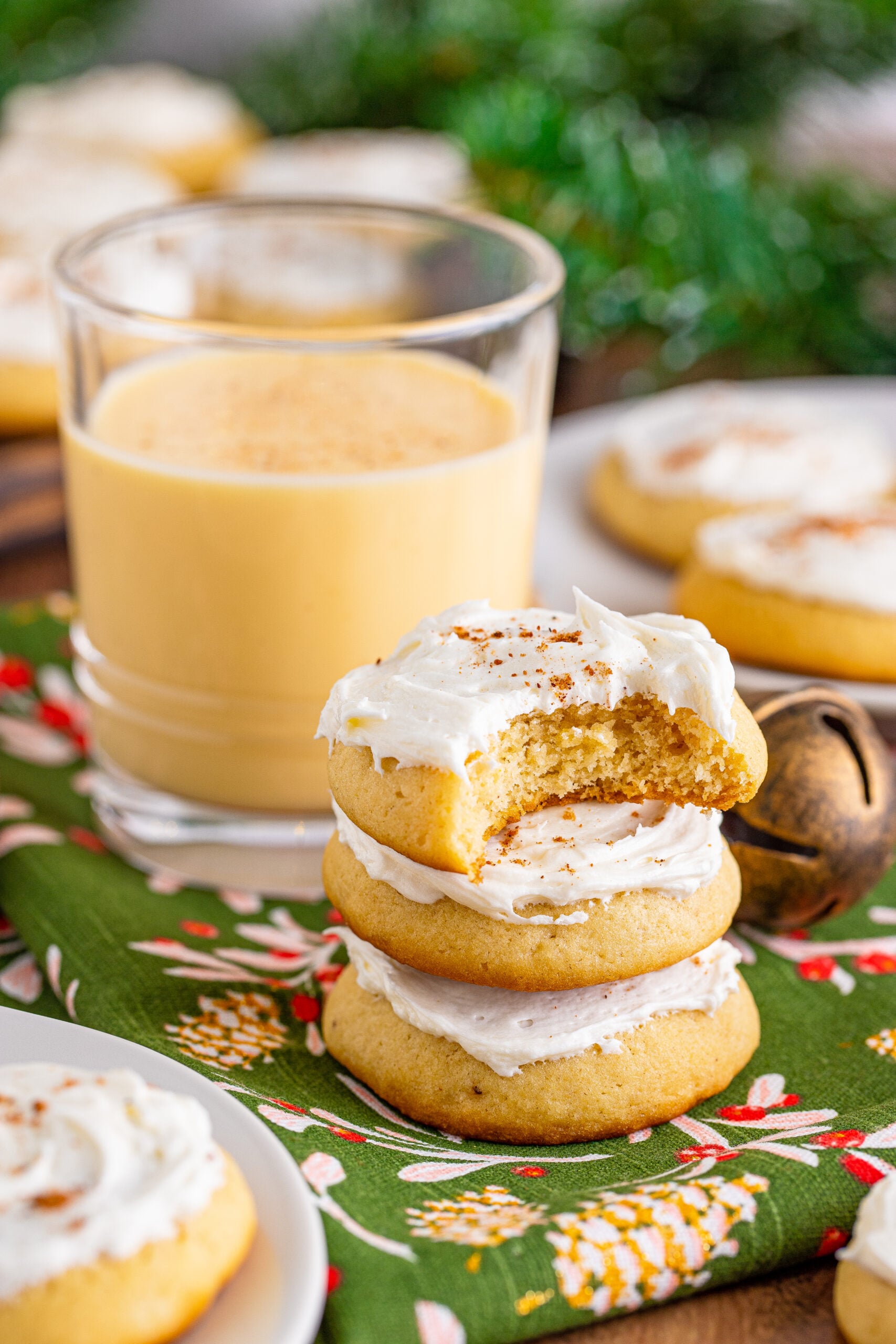 Soft Frosted Eggnog Cookies stacked on a table with a bite missing from the top cookie