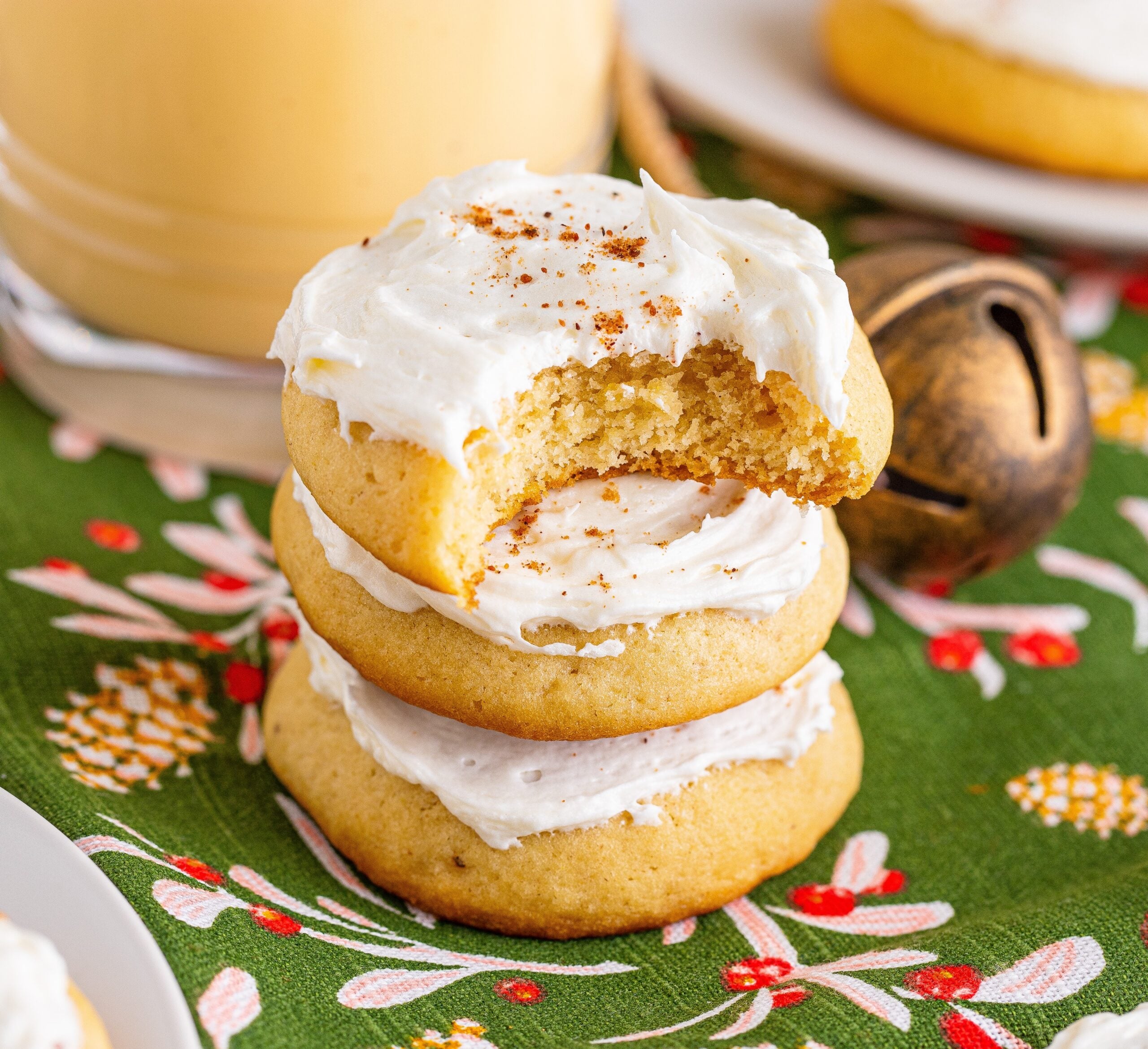 Soft Frosted Eggnog Cookies stacked on a table with a bite missing from the top cookie