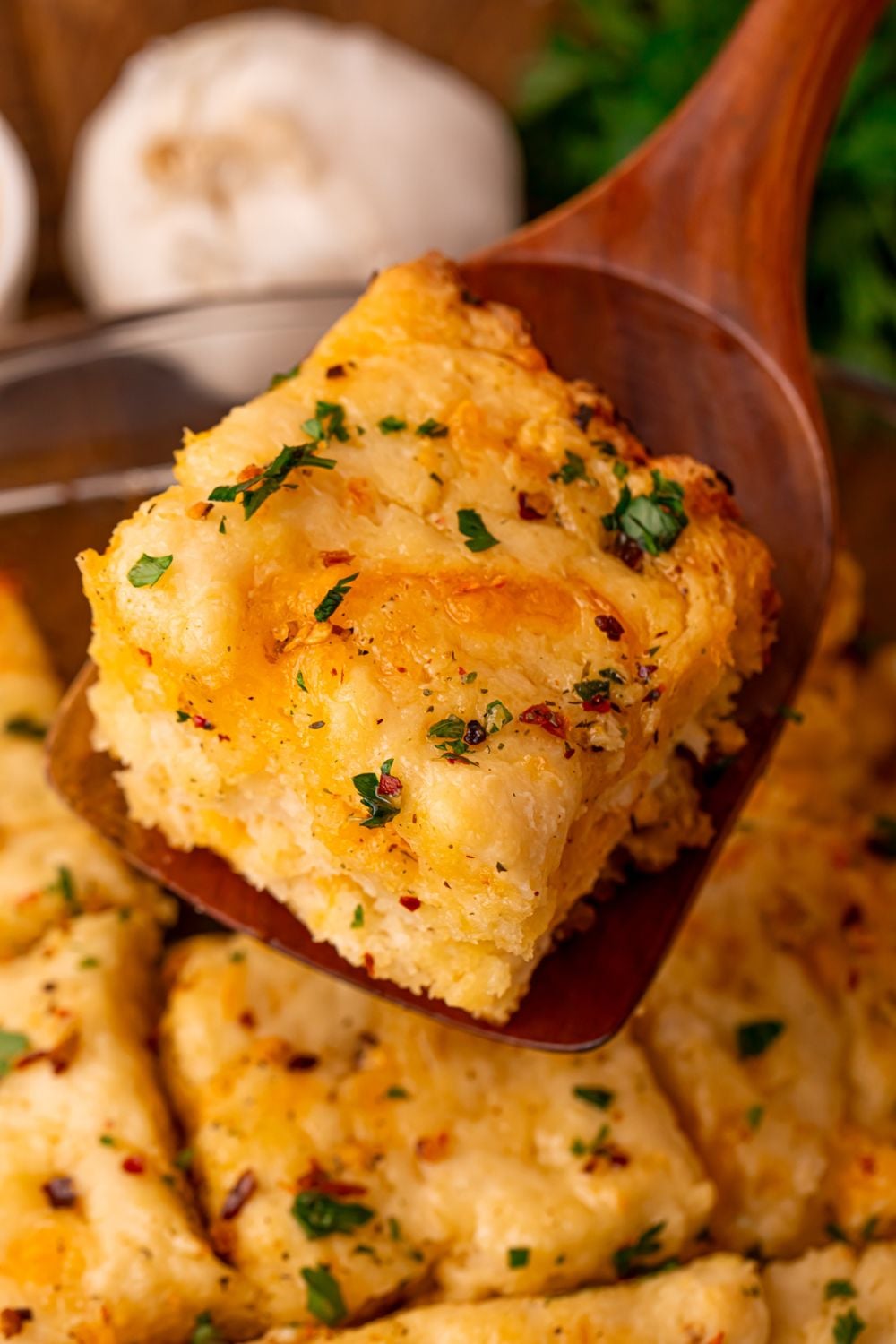 pan full of Cowboy Butter Swim Biscuits with a wooden spoon lifting up one of the biscuits on the table